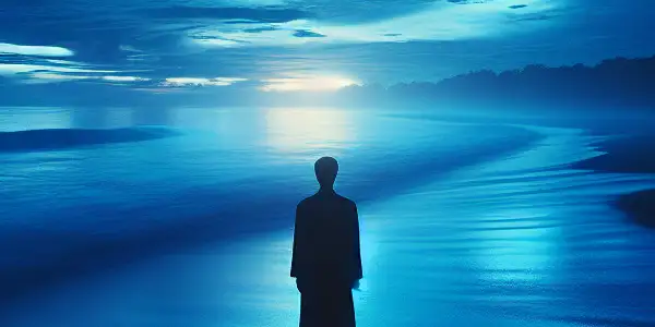 A solitary figure stands on a tranquil beach at twilight, gazing at the deep blue ocean and sky.